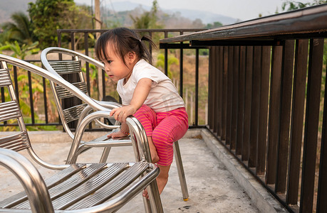 攀爬小孩摄影照片_亚洲小孩试图自己爬下椅子，这对孩子来说很危险。