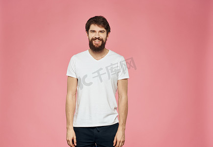 运动休闲裤子摄影照片_粉红色背景中穿着 T 恤和裤子的留着胡子的家伙