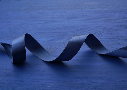 蓝色木质背景上扭曲的深蓝色丝绸细丝带