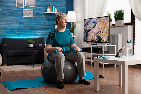 瑞文电脑壁纸摄影照片_穿着运动服的专注老年女性使用平板电脑观看在线健身锻炼
