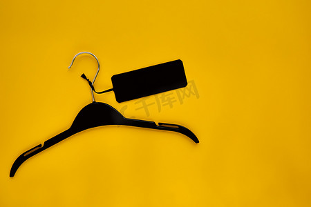 服装海报背景摄影照片_黑色衣架与黄纸背景上隔离的黑纸标签。