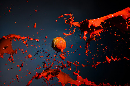 飞溅牛奶液体摄影照片_蓝色背景中的红色油漆飞溅和网球