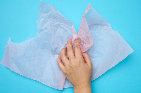 蓝色背景上女手握着粉色折叠包装皱纸