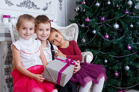 礼盒绿色摄影照片_孩子们坐在圣诞洋红色树下，带着礼盒