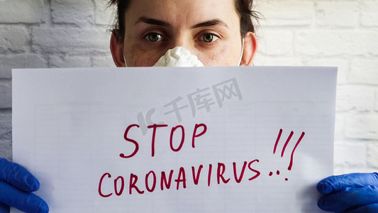 一名戴着防护面具的妇女的肖像，照片中相机特写了一张白纸，上面用红色记号笔写着“阻止冠状病毒”的文字。