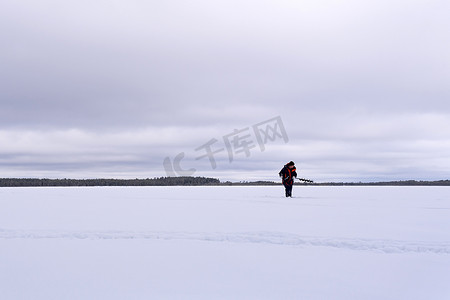 冰钻摄影照片_冬天湖上的渔民用电钻钻冰