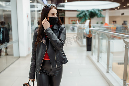 一个戴着医用黑色口罩的女孩沿着购物中心行走。
