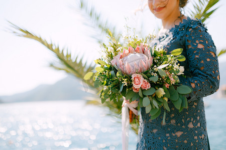 双人结婚登记照摄影照片_身穿时尚灰色连衣裙的新娘站在海边，手里拿着婚礼花束，特写