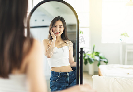 一位年轻女子减肥前穿着大牛仔裤，看着镜子前的身材，很高兴自己减肥成功，露出非常自信的笑容