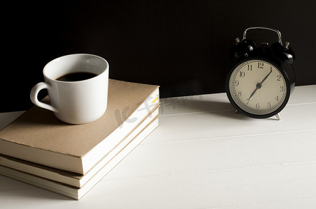 一杯咖啡在书上，白色桌子上有复古闹钟。