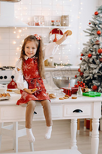 圣诞厨房里一个快乐的小女孩坐在桌子上，手里拿着饼干