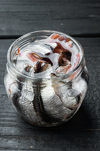 黑色木桌背景上的锡罐海鲜中的凤尾鱼罐头鱼，玻璃罐中的鱼