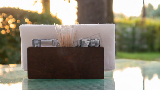 椅子阴影摄影照片_咖啡厅的玻璃桌上放着一个棕色的木制餐巾架和牙签，被阳光照亮。