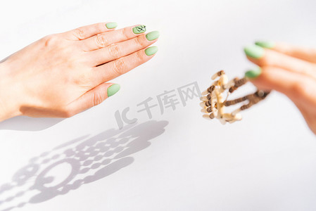 女人的手上有漂亮的绿色指甲，拿着木项链。