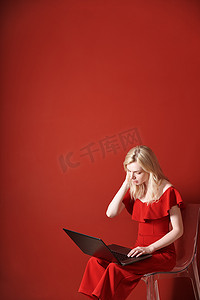 便携式椅子摄影照片_年轻的成年女性坐在椅子上，在笔记本电脑上工作