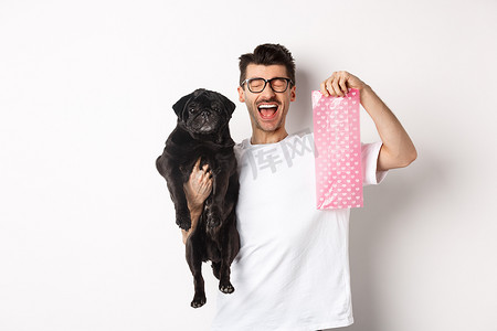 快乐男人、宠物主人的形象，拿着可爱的黑色哈巴狗和狗屎袋，站在白色背景上