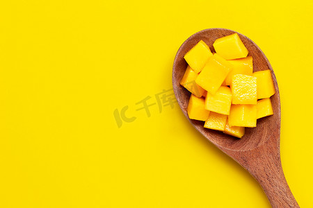 在黄色背景的木勺上切熟的芒果块。