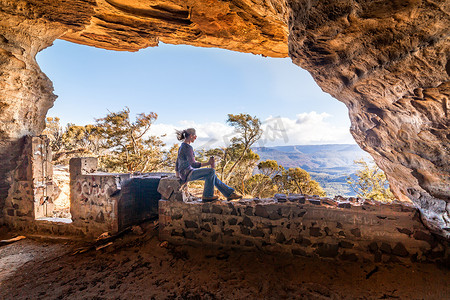 温特沃斯摄影照片_一位女性在洞穴里放松，可以欣赏数英里的悬崖侧景，旅游