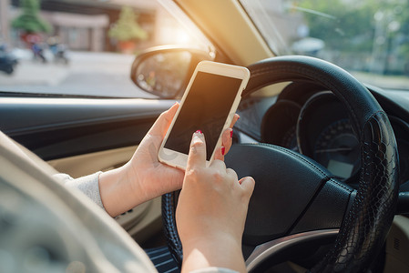 手握手机方向盘摄影照片_年轻女司机使用触摸屏智能手机和手握方向盘在车里。