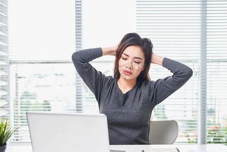 已完成的工作摄影照片_年轻无聊的女人坐在办公室里，坐在笔记本电脑前，感到昏昏欲睡。