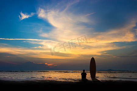 沙滩冲浪板摄影照片_冲浪人的剪影坐在沙滩上的冲浪板上。