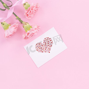 优雅粉色背景摄影照片_美丽、清新优雅的康乃馨花束，配有白色问候感谢礼品卡，隔离在亮粉色背景、顶视图、平躺概念上。