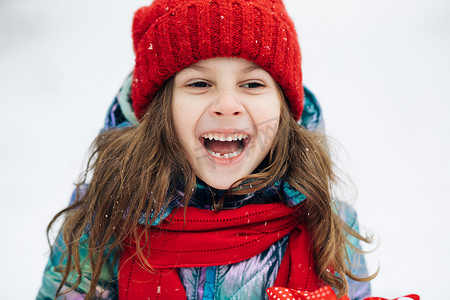 关闭快乐可爱的女孩看着相机，微笑着白雪皑皑的森林的背景。