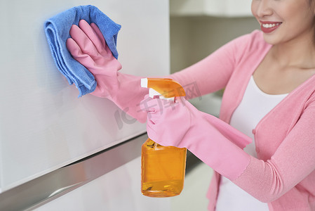 戴防护手套的妇女在室内用抹布清洁冰箱