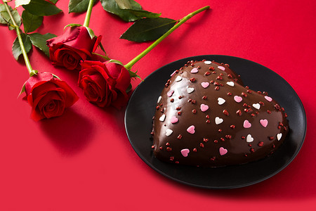 红玫瑰蛋糕摄影照片_情人节或母亲节的心形蛋糕和红玫瑰