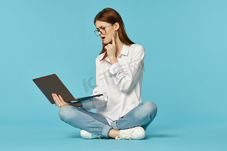 坐在地板上学习学生技术蓝色背景的笔记本电脑的妇女