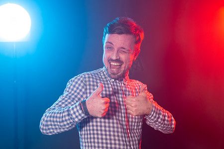 穿着格子衬衫、留着胡子的年轻男子笑着在蓝红色背景的工作室里摆出拇指姿势。