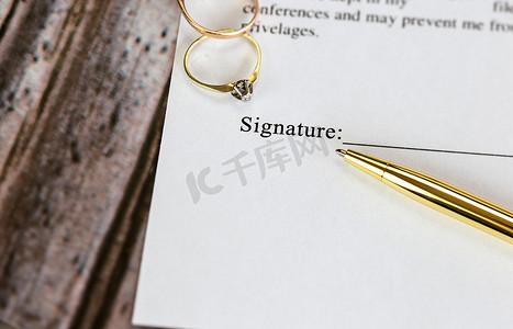 与两个金婚戒指和金笔的婚姻合同、婚前协议、宏观特写、签字、文件、协议概念