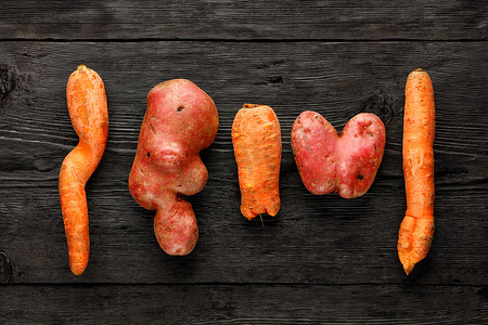 心形丑陋的土豆和黑色木制背景上扭曲的胡萝卜。