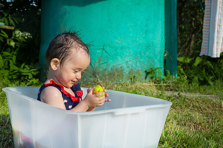 穿着泳衣的一岁半女孩坐在白色浴缸里和黄色小鸭玩耍