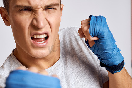 活动浅色背景摄影照片_戴着蓝色手套的运动男拳击手在浅色背景裁剪视图中练习拳击