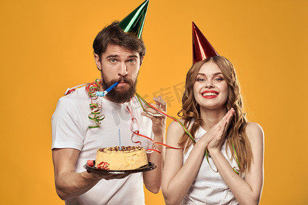 英文版生日快乐摄影照片_快乐的男人和女人，带着生日蛋糕生日帽派对黄色背景