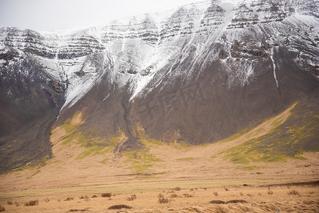 白雪覆盖的灰色山顶，具有绿色和棕褐色的泥土色调和纹理