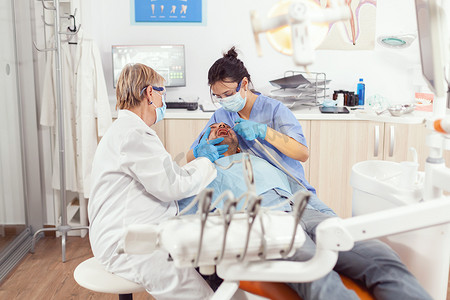 生病的病人坐在口腔科椅子上，而护士正在检查口腔