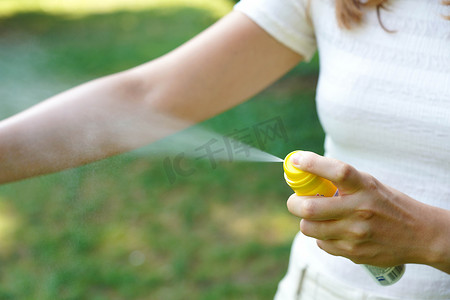 在大自然中徒步旅行时，年轻女子在手臂上涂抹驱蚊剂。