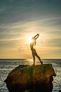女子体操运动员正在海边日落的海滩上训练。