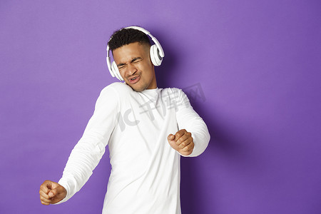 无忧无虑的非洲裔美国人跳舞、用无线耳机听音乐、站在紫色背景上的形象