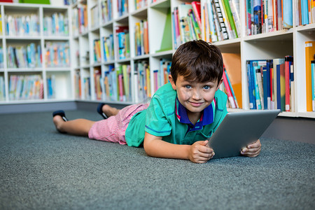 小孩儿看书摄影照片_在学校图书馆使用数字平板电脑的男孩肖像