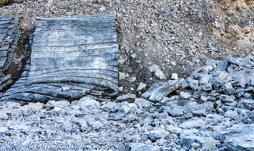 在新筑路工地的爆破岩石区域的一侧关闭照片爆破保护橡胶垫，其中有许多石头。