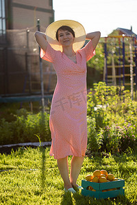 阳光明媚的夏日，戴着帽子和粉色裙子的年轻白人积极女园丁手里拿着装着柠檬的盒子。