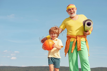 快乐的老人和可爱的小男孩在天空背景下练习运动和健康的生活方式。