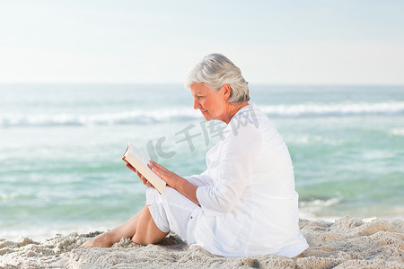 在沙滩上看书的老妇人