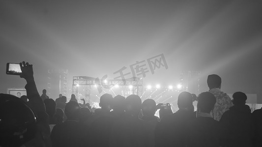 大群快乐的人站在音乐会场地欢呼鼓掌的剪影使用智能手机举起双手面对音乐乐队享受。