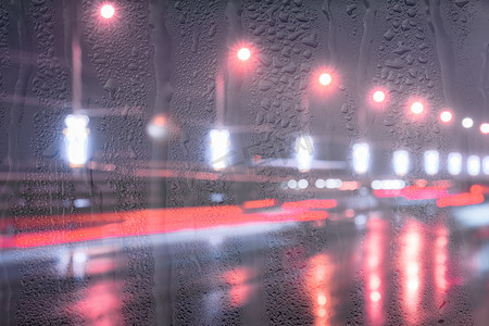 雨中街道摄影照片_行驶中的汽车和灯笼的模糊灯光反射在夜城被雨覆盖的窗户后面潮湿的沥青上。