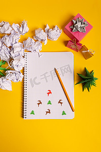 礼品盒和绿色折纸树，黄色书桌、桌子上有记事本。