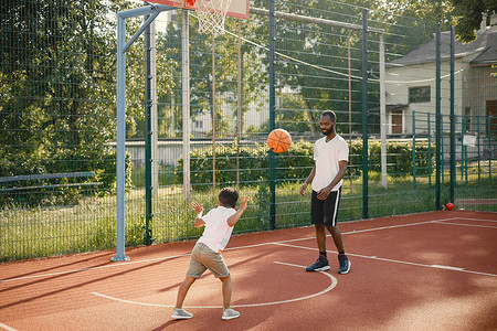 打篮球的的人摄影照片_黑人父亲带着儿子一起在篮球场打篮球